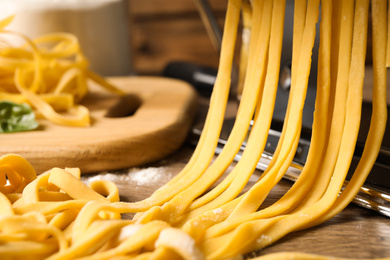 Photo of Pasta maker machine with dough on wooden table, closeup