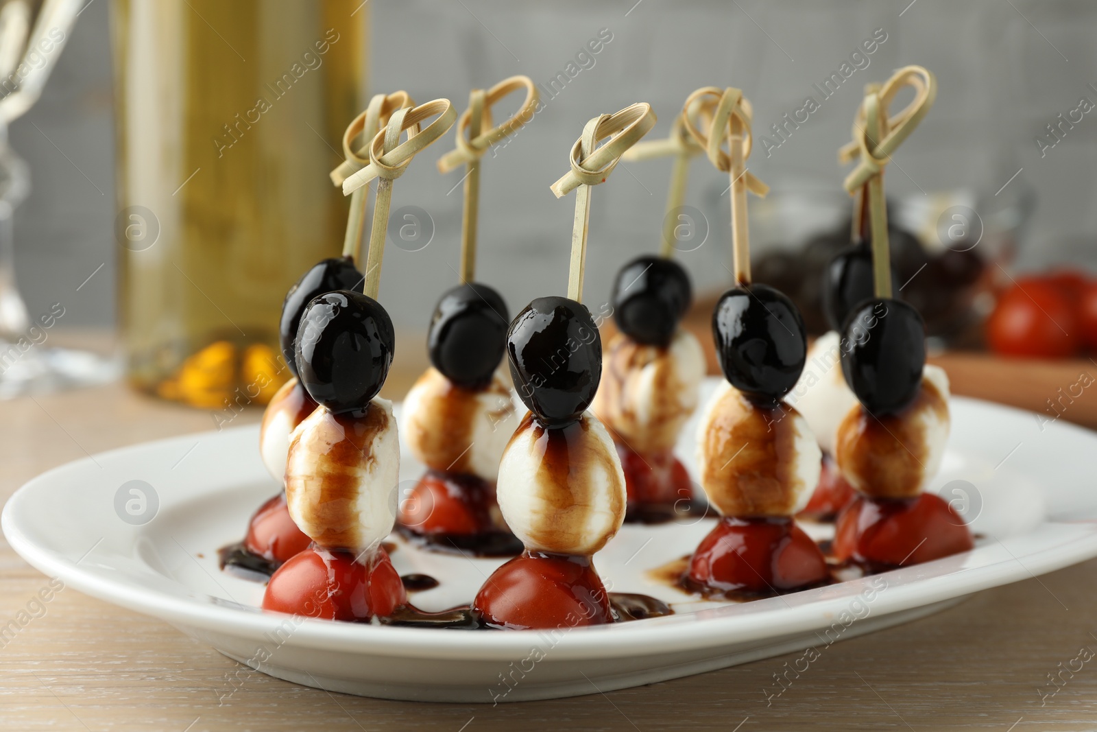 Photo of Tasty canapes with black olives, mozzarella and cherry tomatoes on light wooden table, closeup