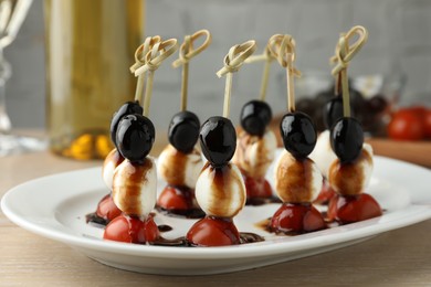 Tasty canapes with black olives, mozzarella and cherry tomatoes on light wooden table, closeup