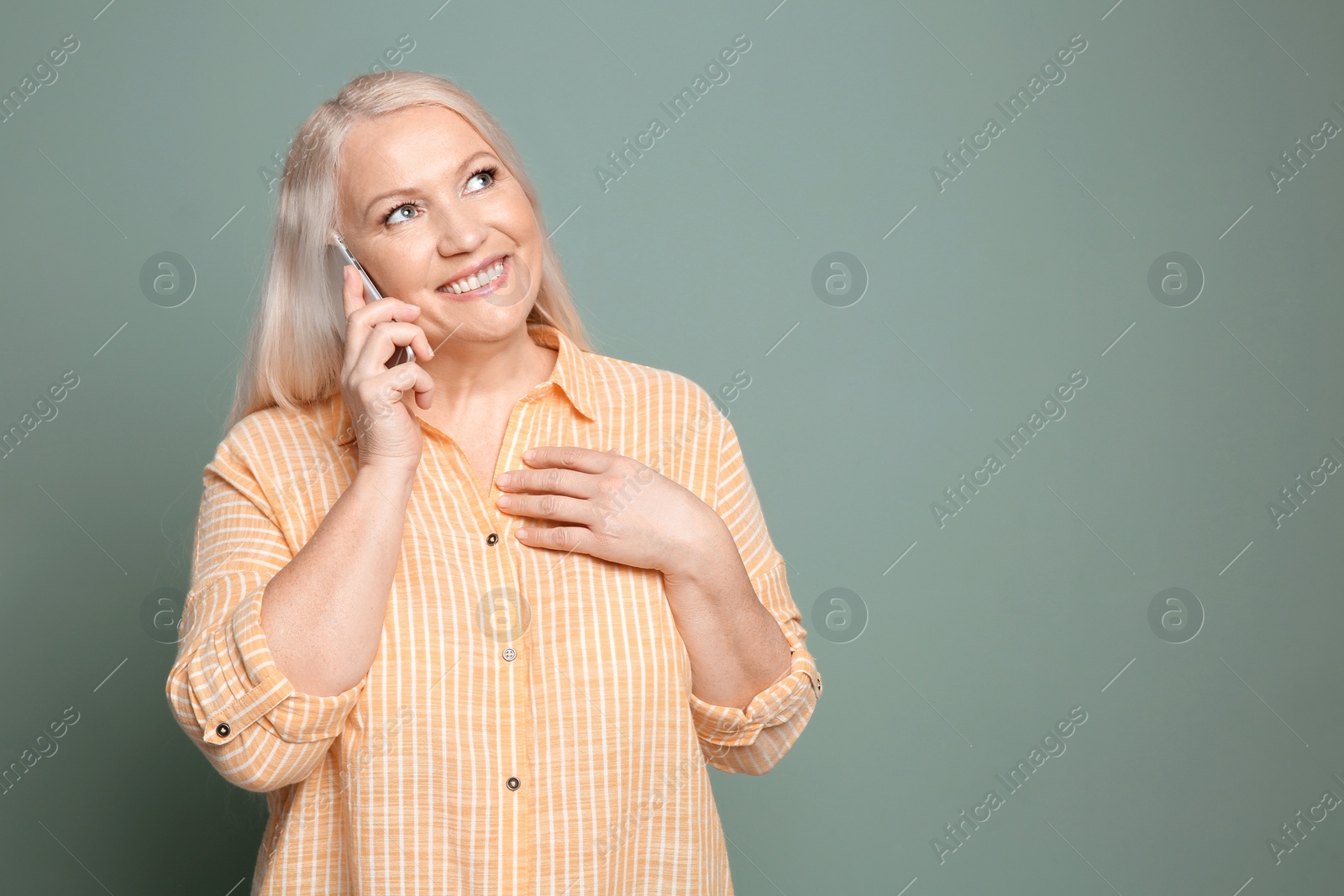 Photo of Mature woman talking on mobile phone against color background