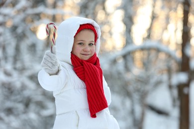 Cute little girl with candy cane in winter park, space for text