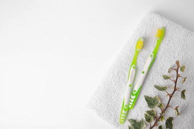 Photo of Light green toothbrushes, terry towel and ivy on white background, top view. Space for text