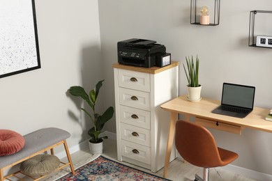 Photo of Modern printer on chest of drawers near wooden table indoors