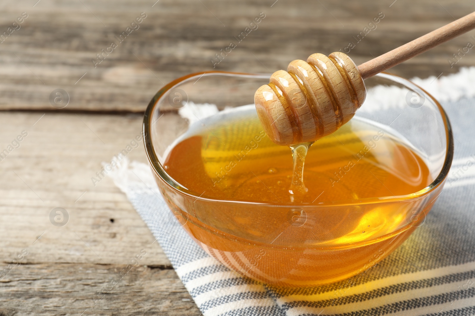 Photo of Delicious honey flowing down from dipper into bowl on wooden table, closeup