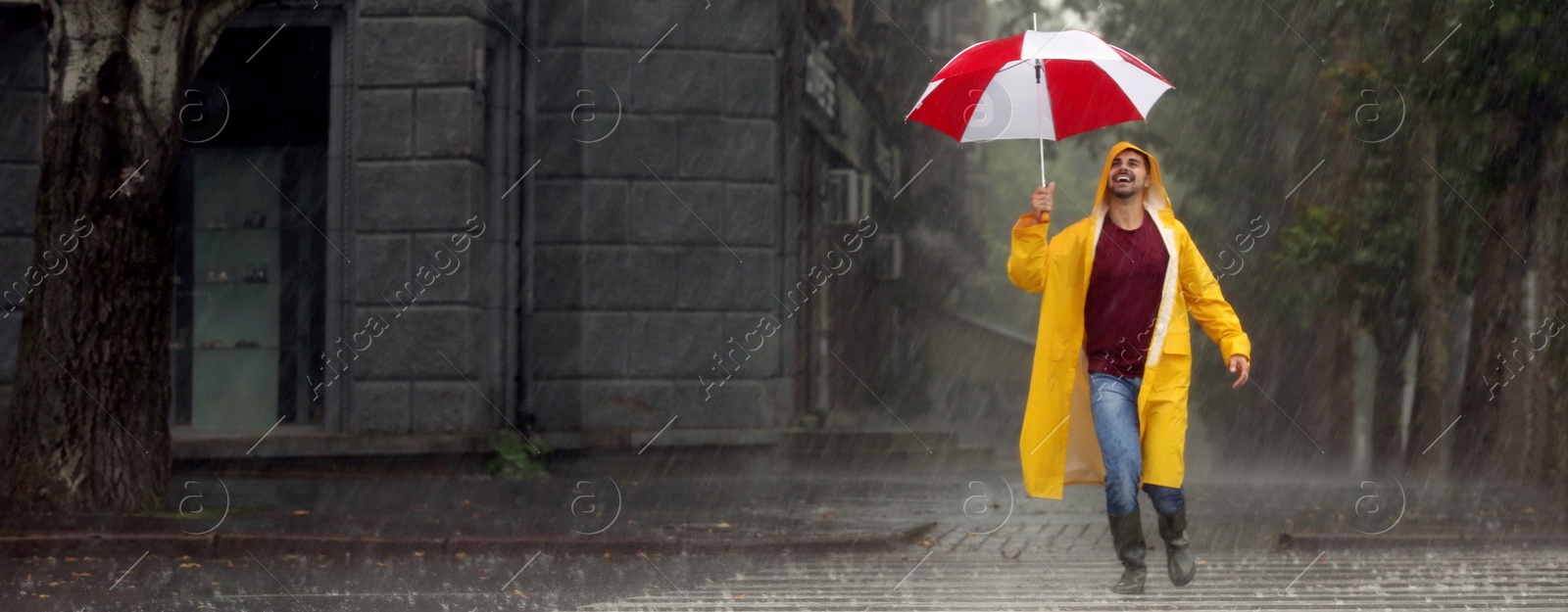 Image of Autumn season. Happy young man with colorful umbrella outdoors on rainy day. Banner design