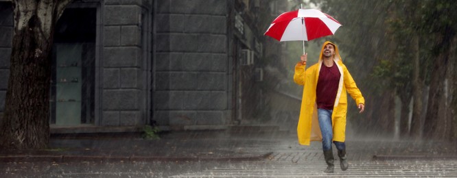 Image of Autumn season. Happy young man with colorful umbrella outdoors on rainy day. Banner design