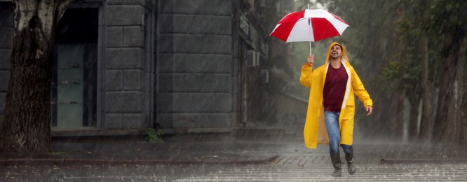 Autumn season. Happy young man with colorful umbrella outdoors on rainy day. Banner design