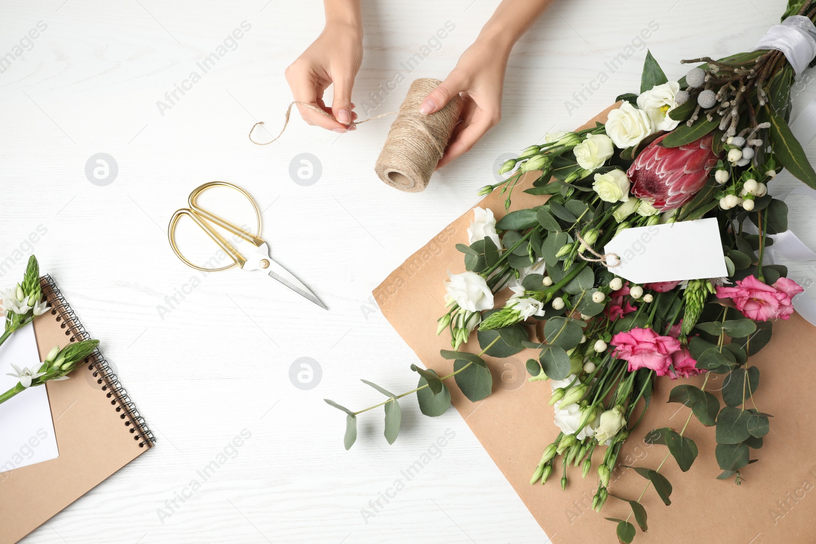 Photo of Florist making beautiful bouquet at white wooden table, top view