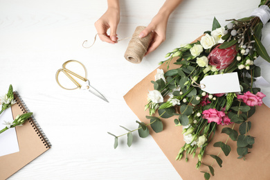 Photo of Florist making beautiful bouquet at white wooden table, top view