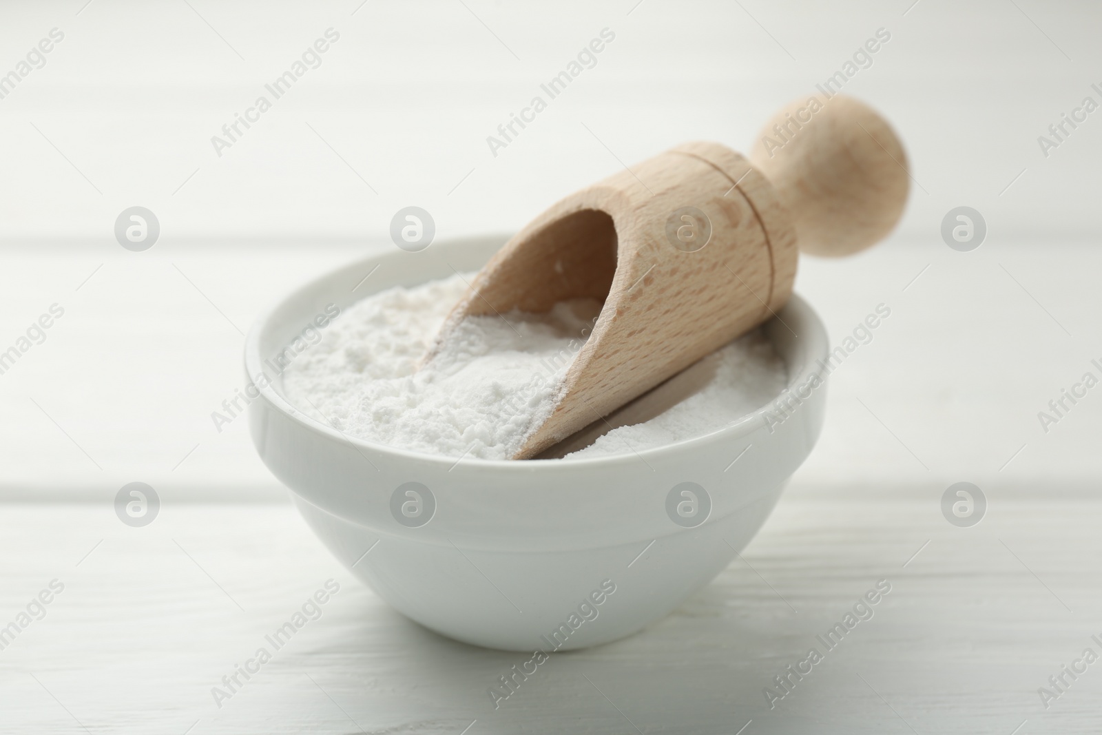 Photo of Baking powder in bowl and scoop on white wooden table, closeup