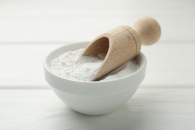 Photo of Baking powder in bowl and scoop on white wooden table, closeup