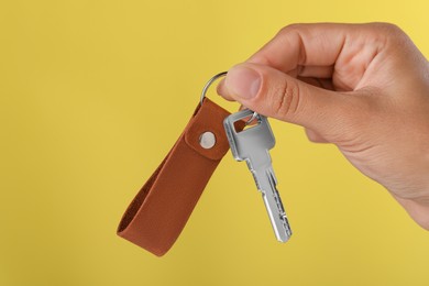 Photo of Woman holding key with leather keychain on yellow background, closeup