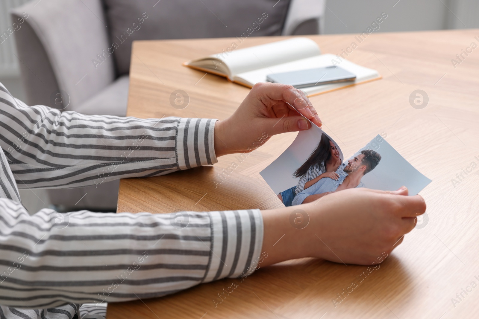 Photo of Woman ripping photo at wooden table in room, closeup. Divorce concept