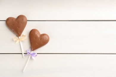 Photo of Chocolate heart shaped lollipops on white wooden table, flat lay. Space for text