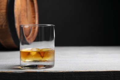 Photo of Glass of tasty whiskey on light gray wooden table, space for text