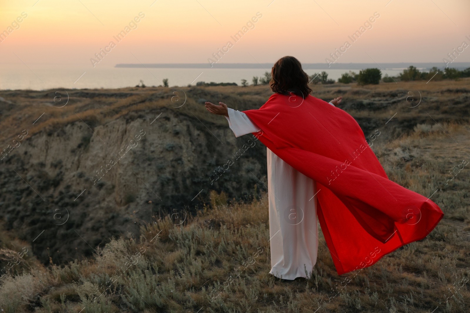 Photo of Jesus Christ raising hands on hills at sunset, back view. Space for text