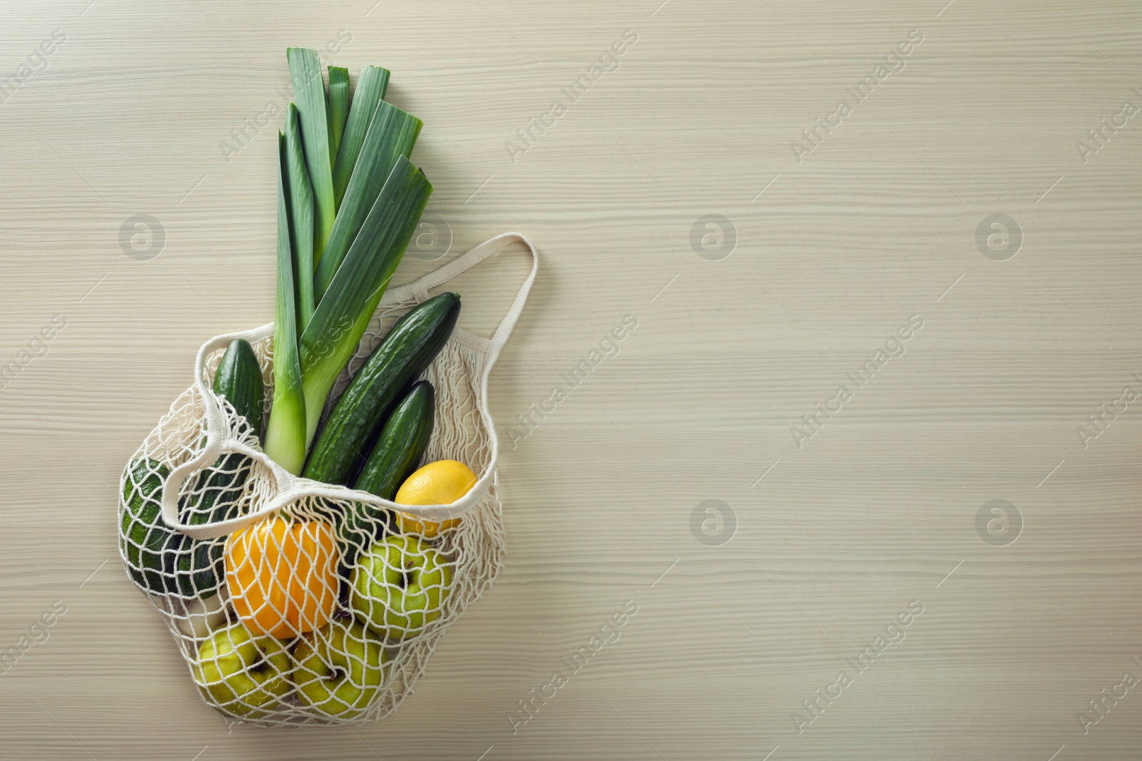 Photo of Net bag with vegetables and fruits on wooden table, top view. Space for text