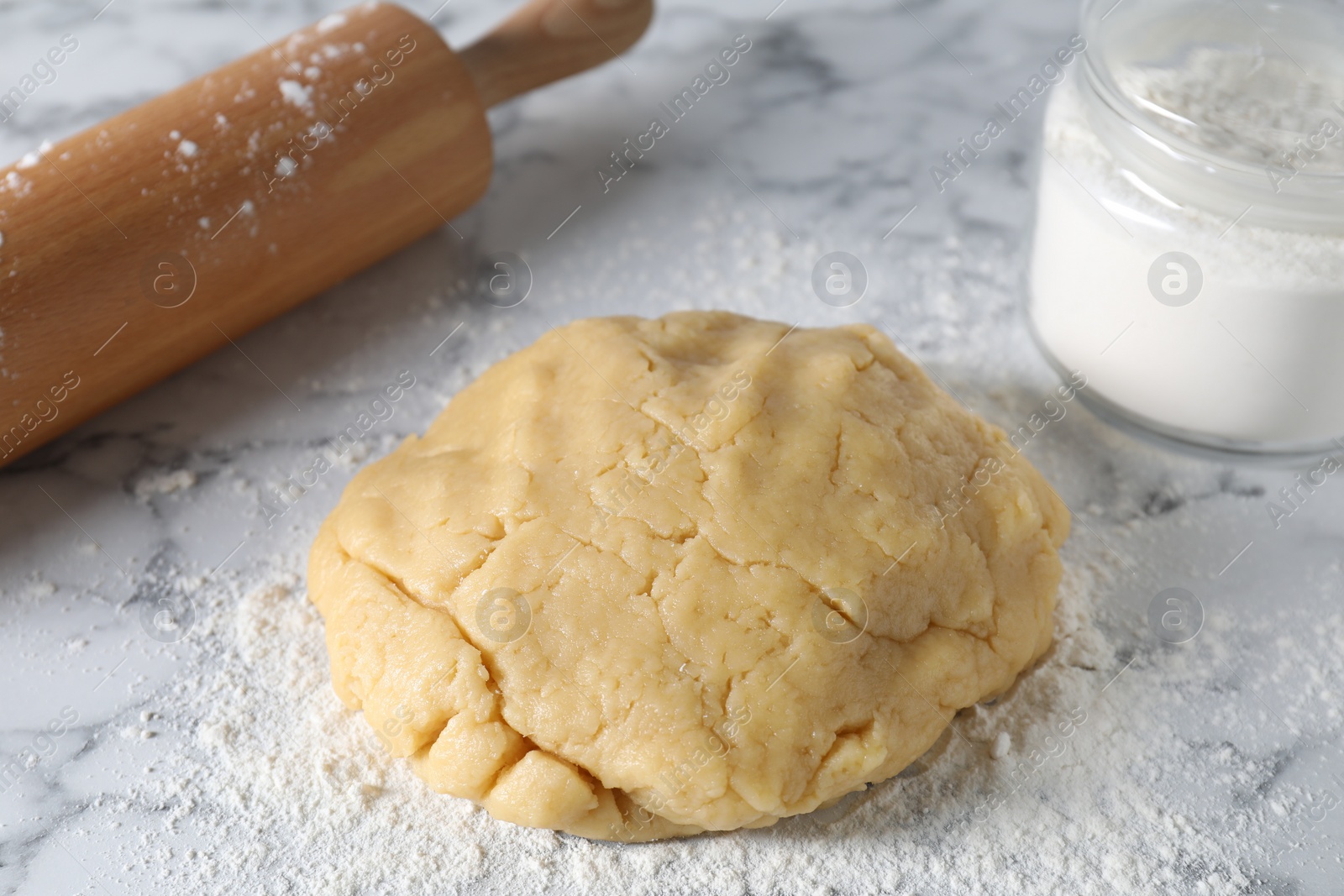 Photo of Making shortcrust pastry. Raw dough, flour and rolling pin on white marble table