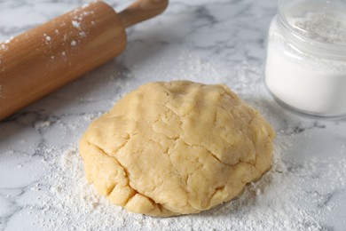 Photo of Making shortcrust pastry. Raw dough, flour and rolling pin on white marble table