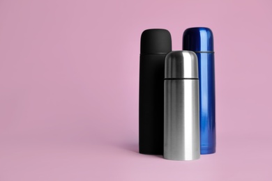 Photo of Stylish thermo bottles on pink background, space for text