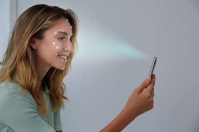 Young woman unlocking smartphone with facial scanner indoors. Biometric verification