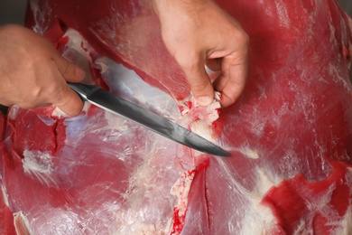 Photo of Butcher cutting fresh raw meat in shop, closeup