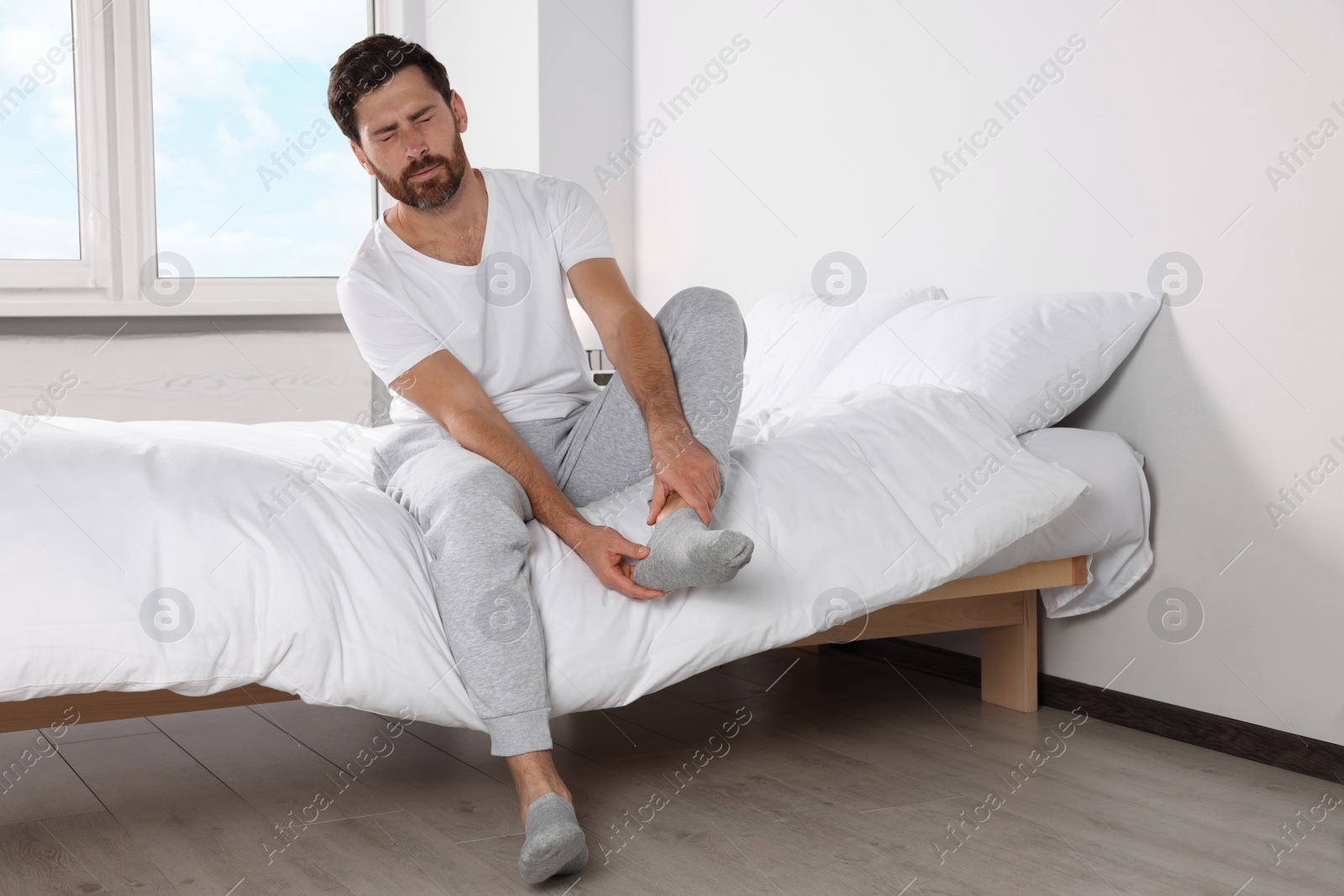 Photo of Man suffering from leg pain on bed at home