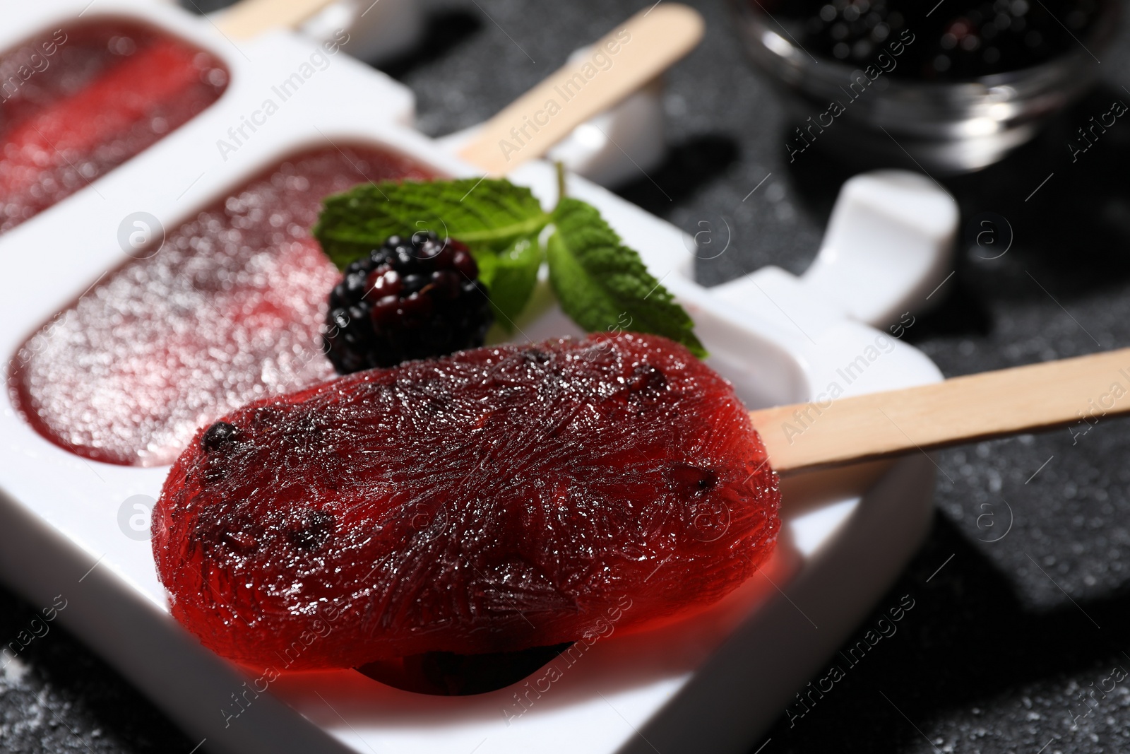 Photo of Mold with tasty blackberry ice pops on dark textured table, closeup. Fruit popsicle