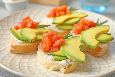 Photo of Tasty sandwiches with fresh sliced salmon fillet and avocado on plate, closeup