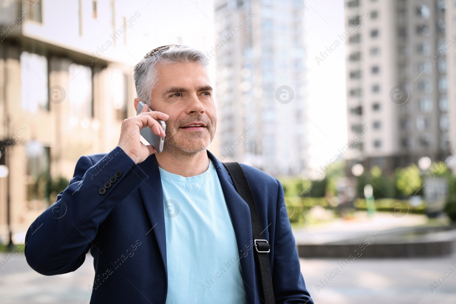 Photo of Portrait of handsome mature man talking on phone in city center. Space for text