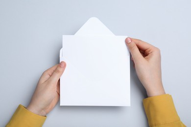 Photo of Woman taking card out of envelope on light grey background, top view