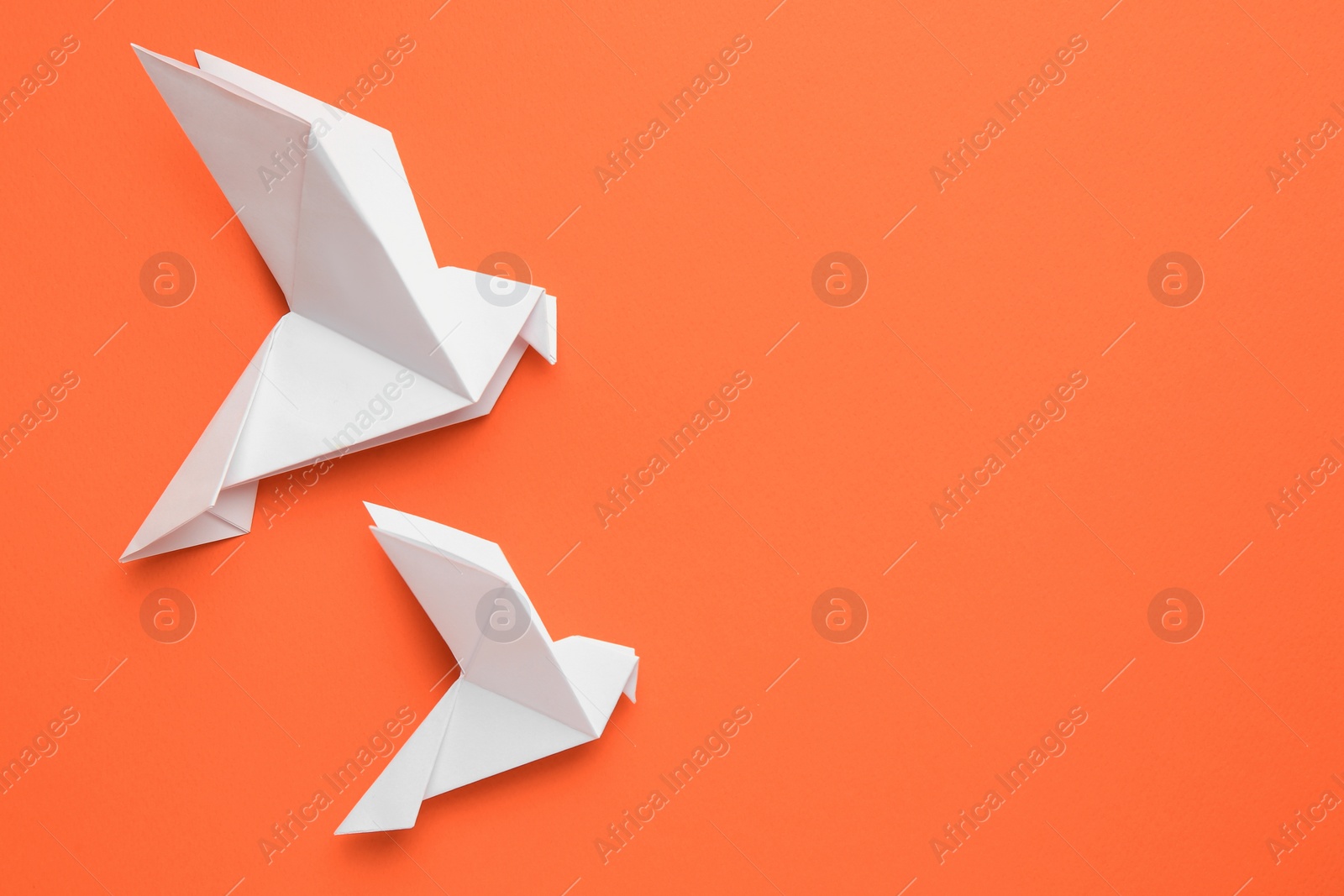 Photo of Beautiful white origami birds on orange background, flat lay. Space for text