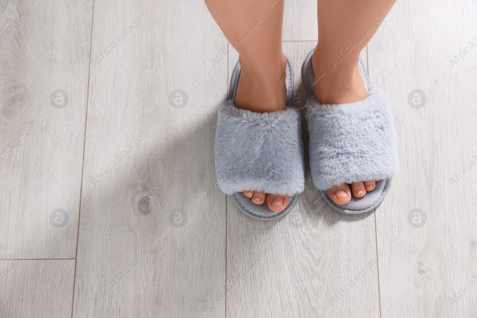 Photo of Woman in soft slippers on white wooden floor, closeup. Space for text