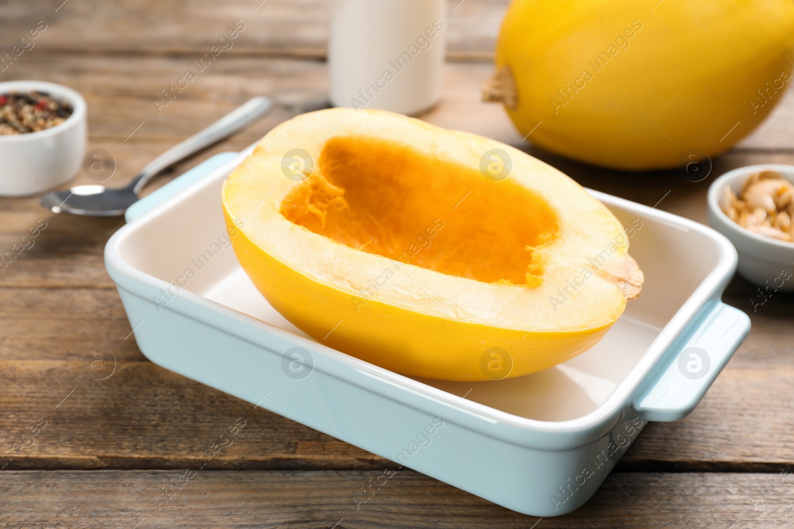 Photo of Raw spaghetti squash half in baking dish on wooden table