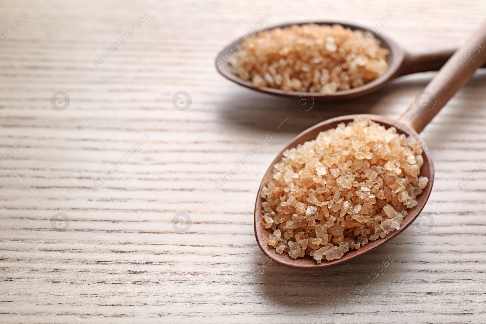 Photo of Spoons of brown sea salt on wooden table, closeup with space for text. Spa treatment