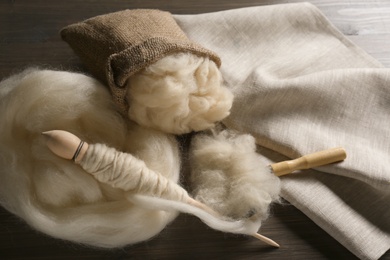 Soft white wool, spindle and comb on wooden table