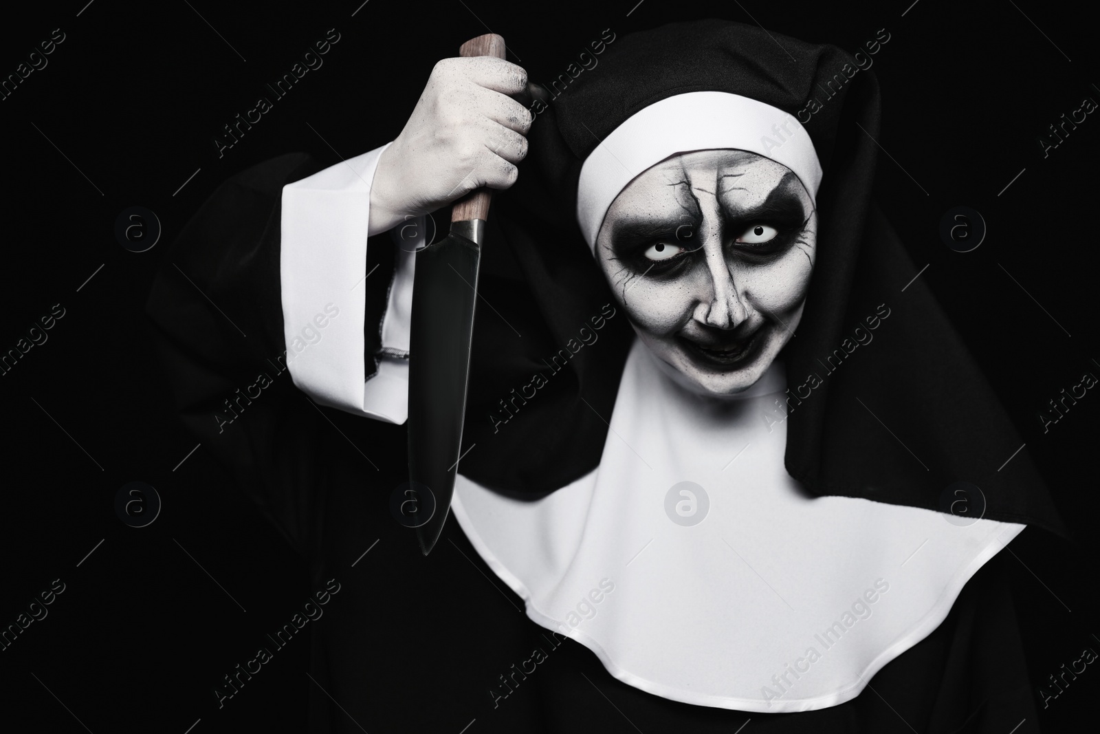 Photo of Scary devilish nun with knife on black background. Halloween party look