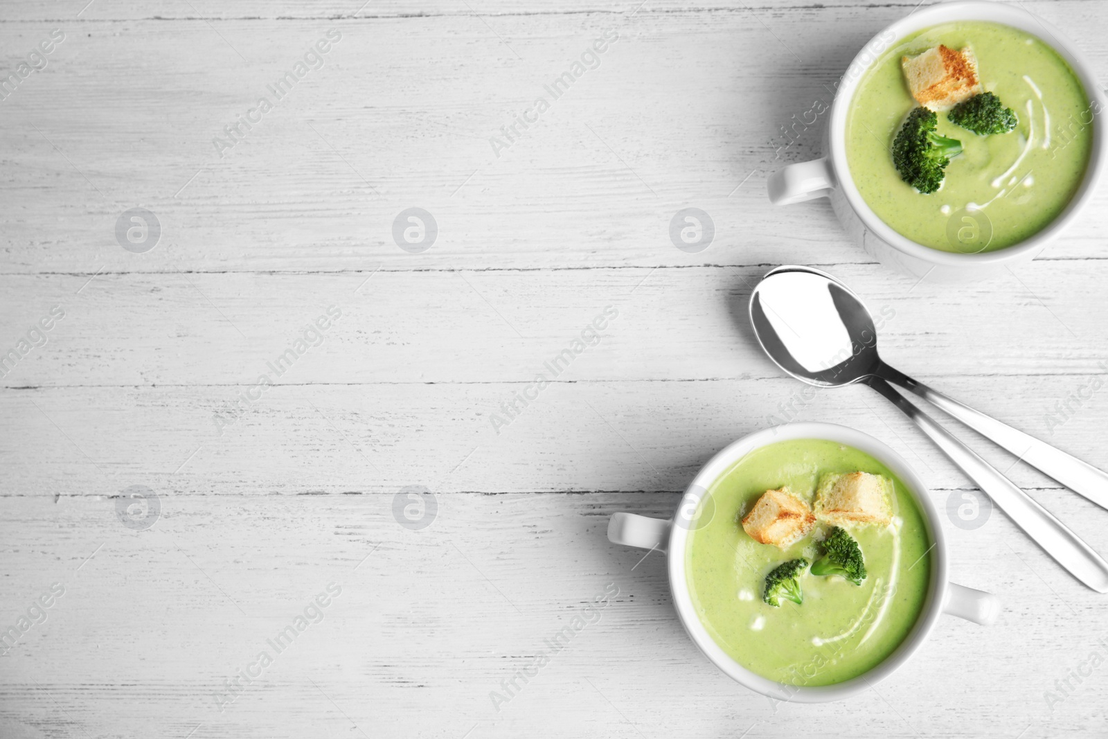 Photo of Delicious broccoli cream soup with croutons served on white wooden table, flat lay. Space for text