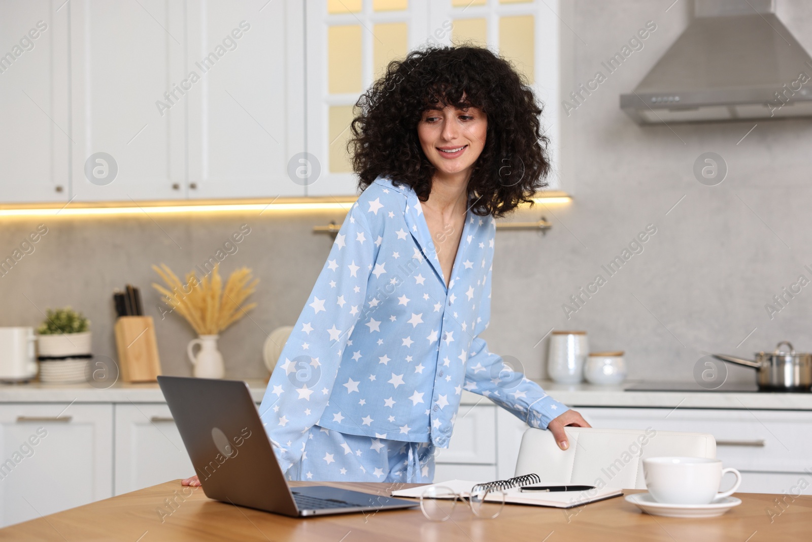Photo of Beautiful young woman in stylish pyjama at wooden table in kitchen