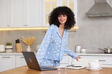 Beautiful young woman in stylish pyjama at wooden table in kitchen