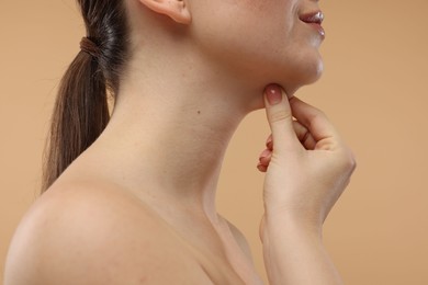 Woman touching her chin on beige background, closeup