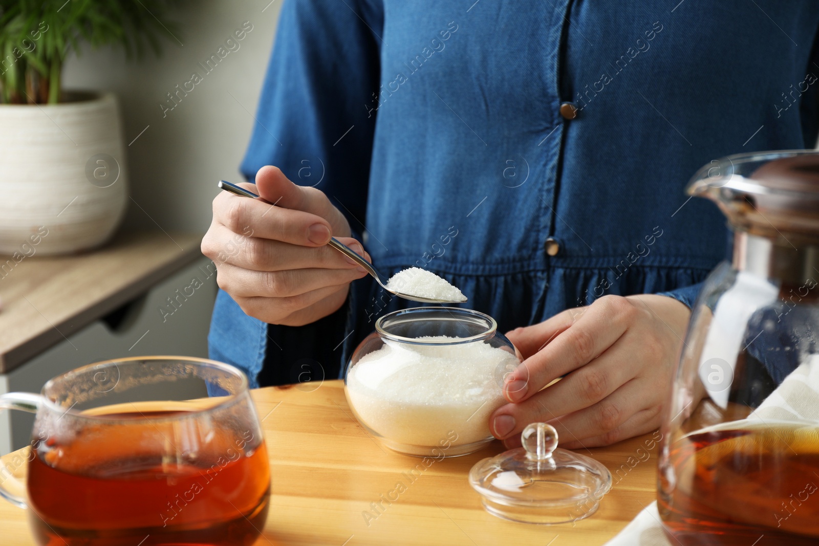 Photo of Woman adding sugar into aromatic tea at wooden table indoors, closeup