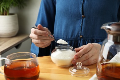 Woman adding sugar into aromatic tea at wooden table indoors, closeup