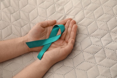 Photo of Woman holding teal awareness ribbon on textile background, closeup. Space for text
