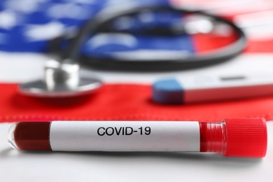 Photo of Test tube with blood sample and stethoscope on American flag, closeup. Coronavirus pandemic in USA