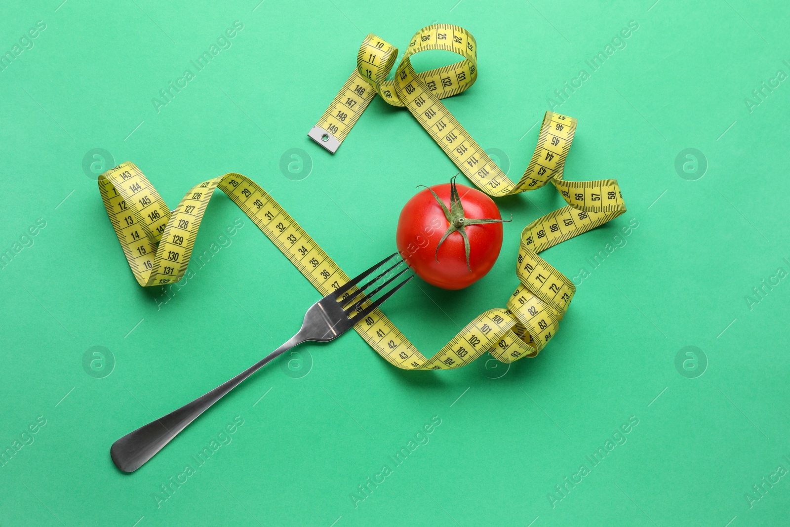 Photo of Tomato, fork and measuring tape on green background, flat lay. Diet concept