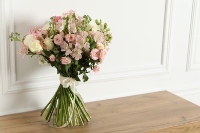 Photo of Beautiful bouquet of fresh flowers on wooden table near white wall, space for text