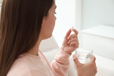 Young woman with glass of water taking pill at home, closeup