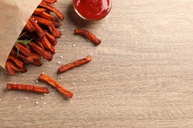 Photo of Paper bag with tasty sweet potato fries and sauce on wooden table, flat lay. Space for text