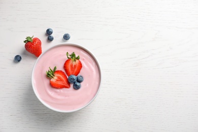 Photo of Bowl with yogurt and berries on wooden background, top view